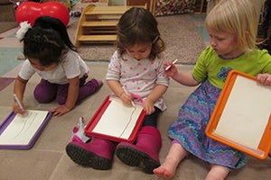 Three friends learning to draw a tree in the Toddler Room at the Co-op Family Center