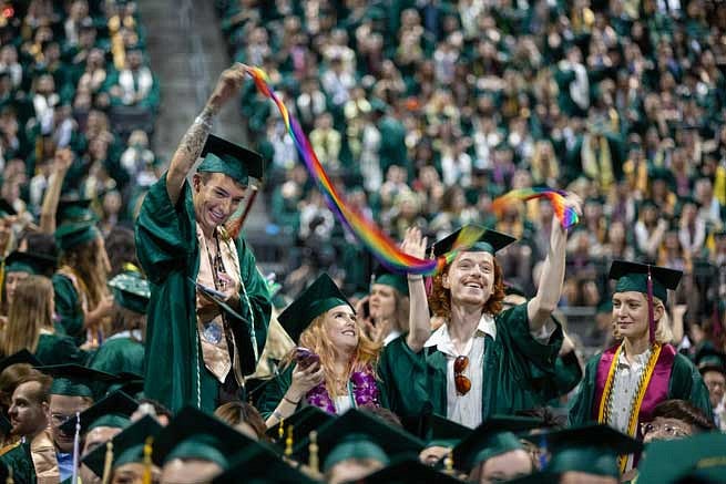 Two graduates holding a rainbow banner during the commencement ceremony Two graduates holding a rainbow banner during the commencement ceremony