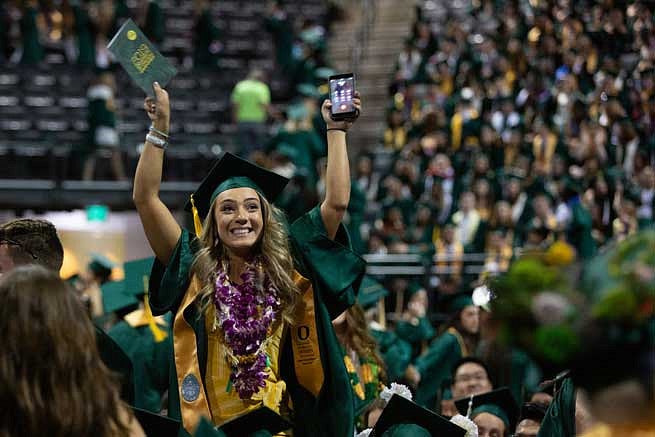 A graduate gesturing to friends and family in the stands during the commencement ceremony A graduate gesturing to friends and family in the stands during the commencement ceremony