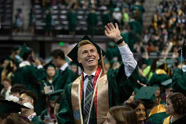 A graduate waving to the stands during the commencement ceremony A graduate waving to the stands during the commencement ceremony
