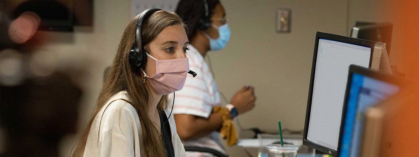 Two Corona Corps student staff members wearing masks while working at computers