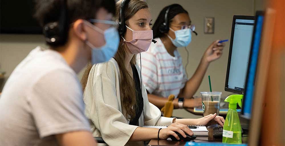 Members of the Corona Corps working at computers while wearing masks