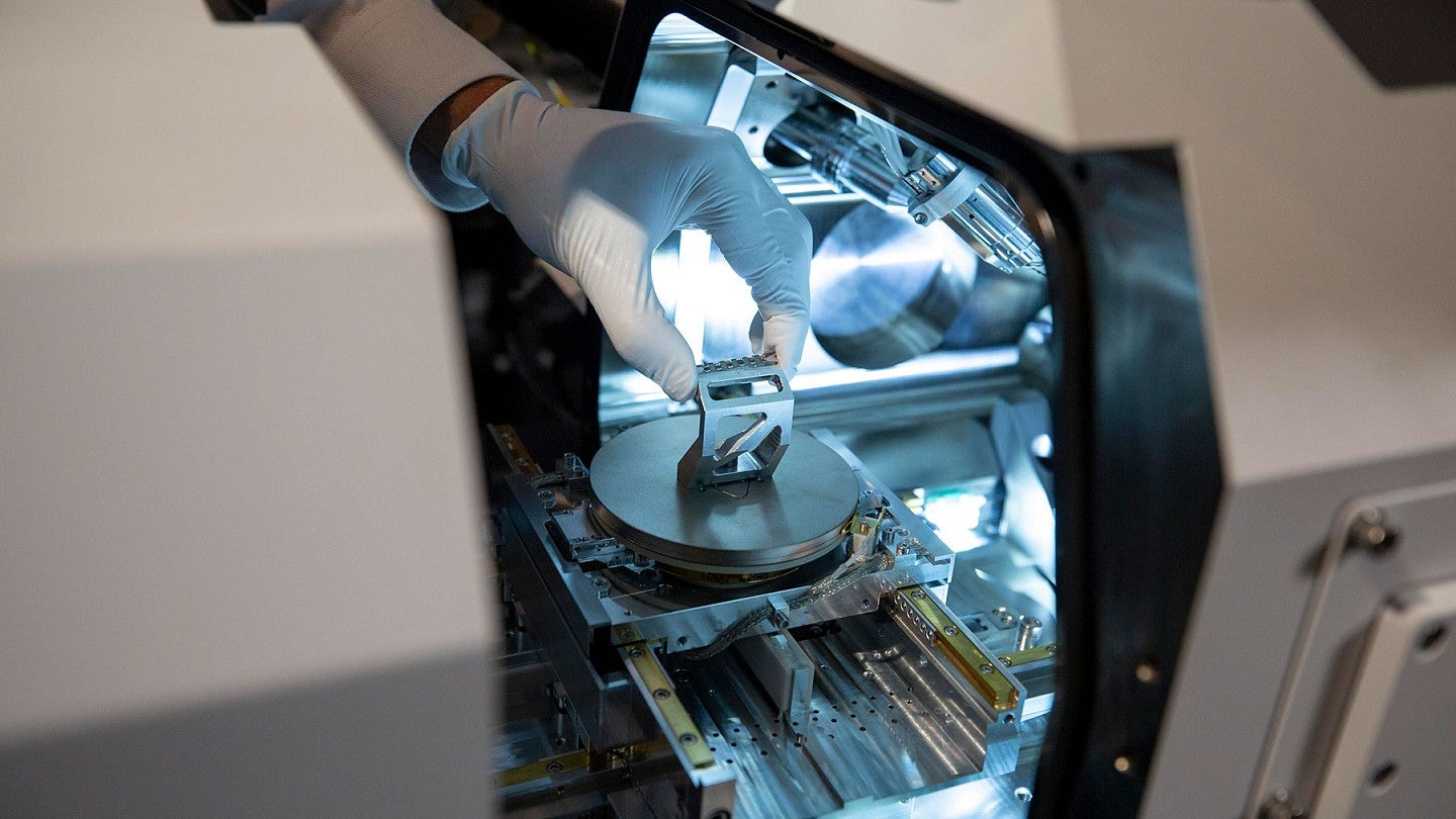 A gloved hand placing a small item into a scientific instrument