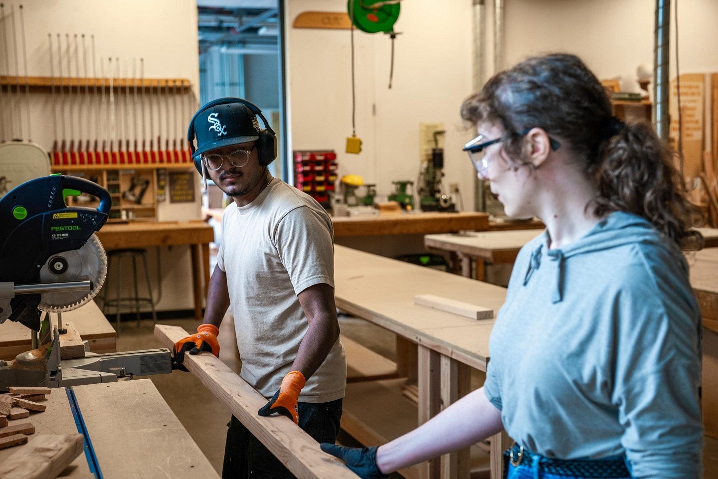 Two students in a woodshop helping to move a 2-by-4 over to a chop saw during the Bruton Design Intensive