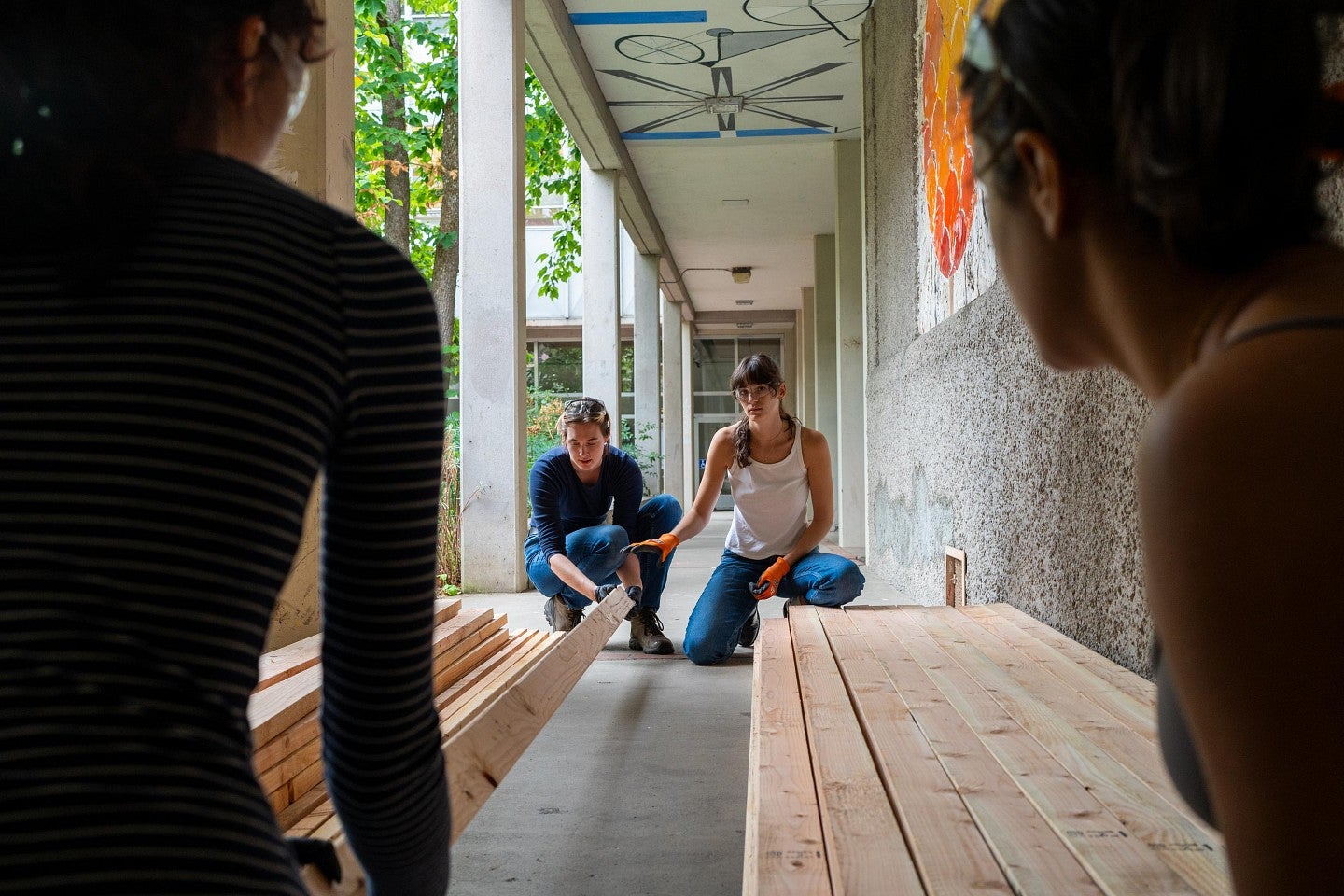 Four students laying out 2-by-4 boards in a breezeway of the Lawrence Hall Courtyard during the Bruton Design Intensive