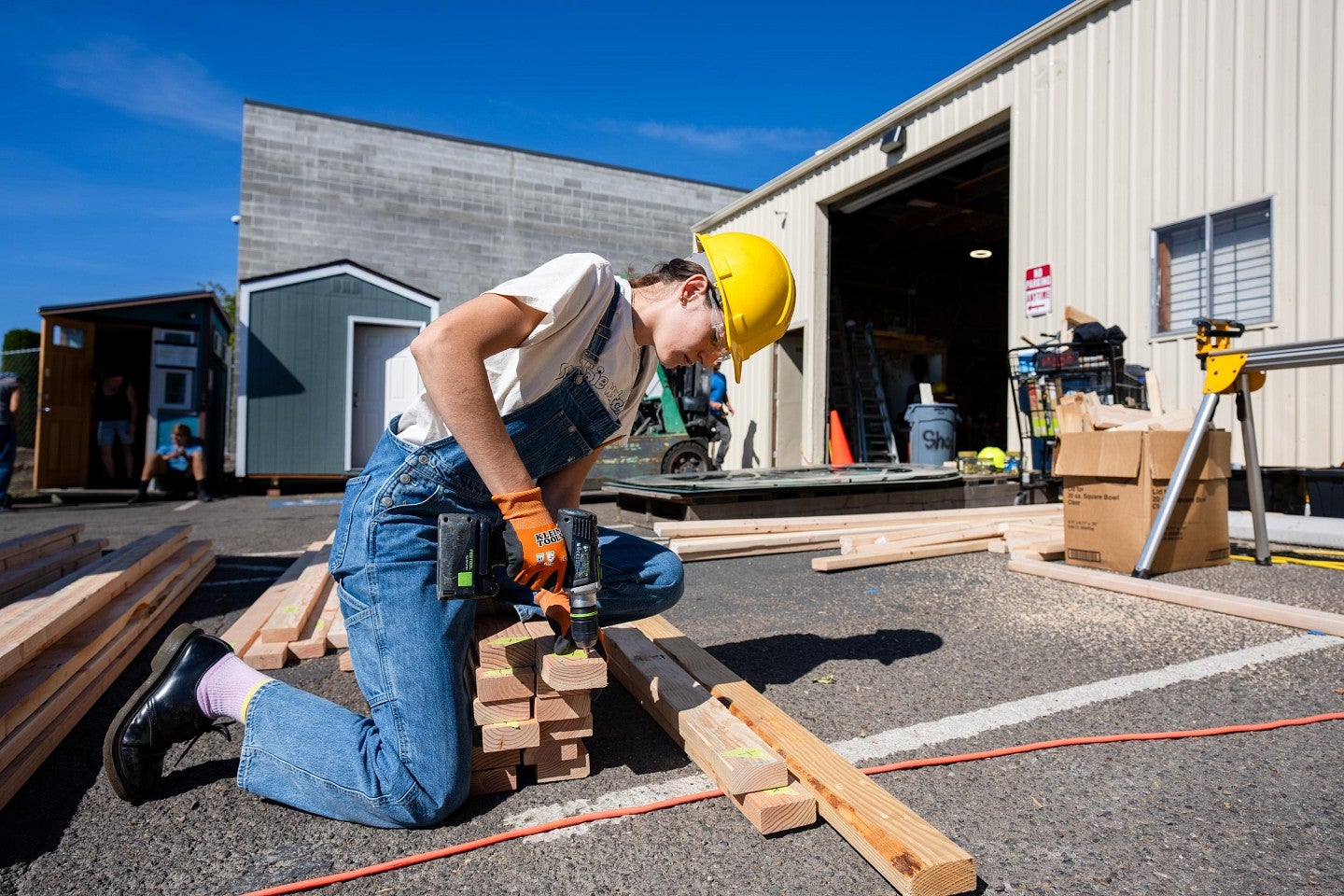 A student using a battery powered drill on a stack of 2-by-4s outside during the Bruton Design Intensive