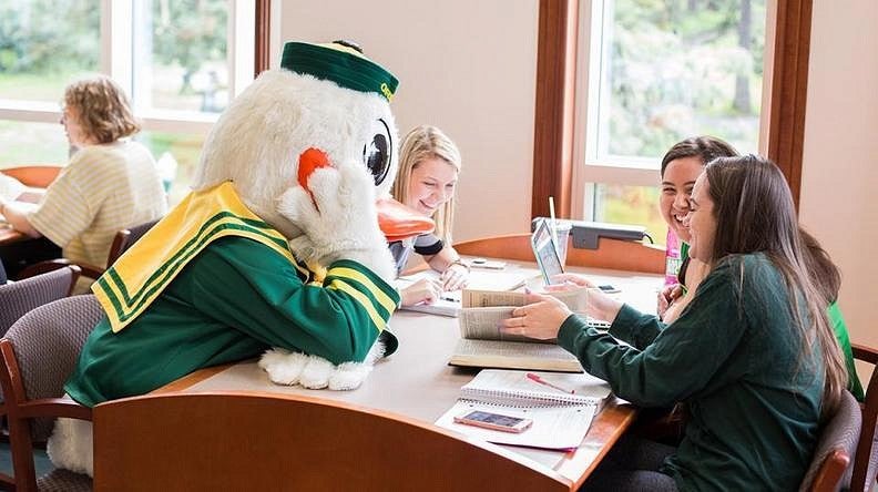 The Duck sitting at a table and listening to three students