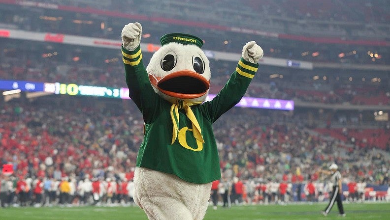 The Duck walking across a football field raising his fists to the crowd.