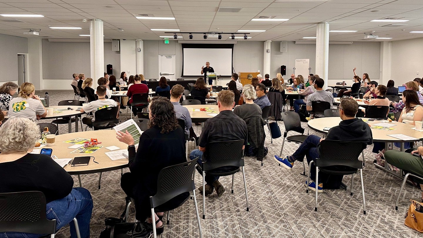 UP Portland employees sitting at round tables during an orientation session with a speaker in the center of the background addressing the crowd