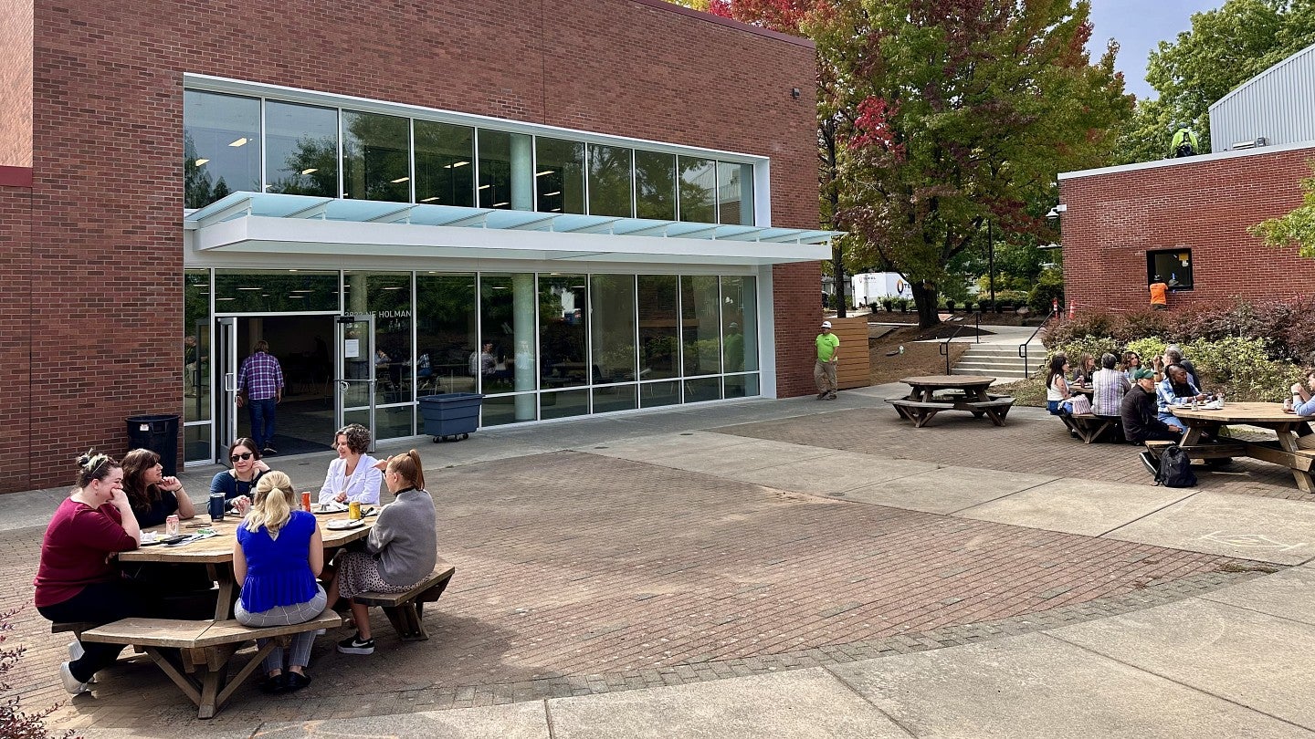 A group of UO Portland employees eating lunch together at an outdoor table in a courtyard in the campus center