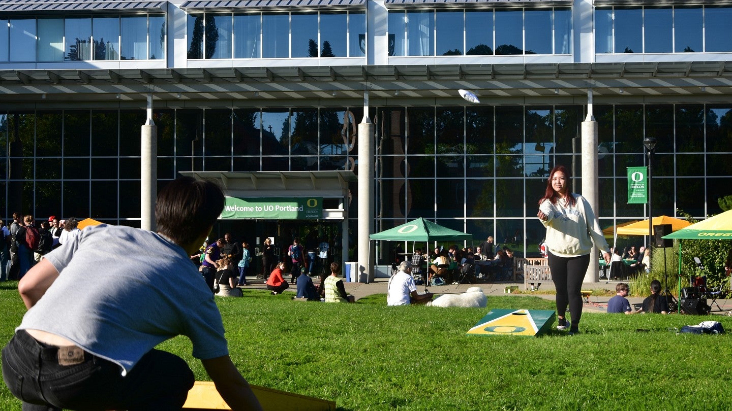 Two students playing cornhole on the lawn outside the UO Portland campus center building