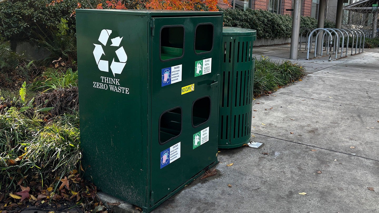 Green bins for trash and recycling on the UO campus, bearing an icon that says “think zero waste.”