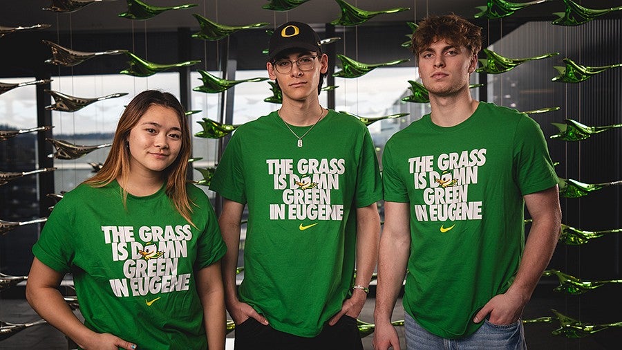 Three students wearing green tshirts that say The Grass is Damn Green in Eugene