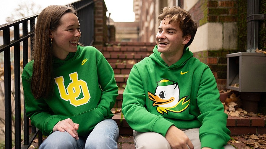 A female and male student laughing and sitting on stairs outside a building