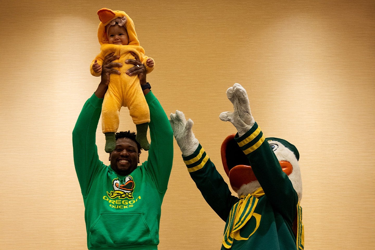 a small child in a duck costume is held aloft by her father while the Duck also reaches up