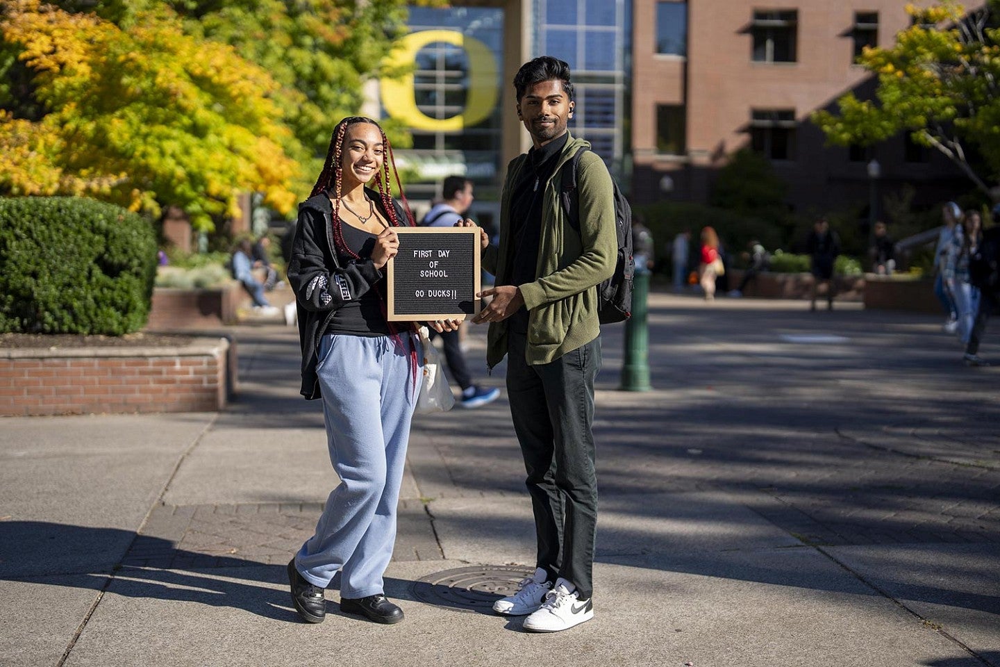 two students in front of the Lundquist College of Business holding a sign that says First Day of School Go Ducks!!