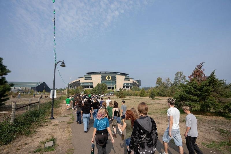 students crossing a bridge with Autzen Stadium in the background