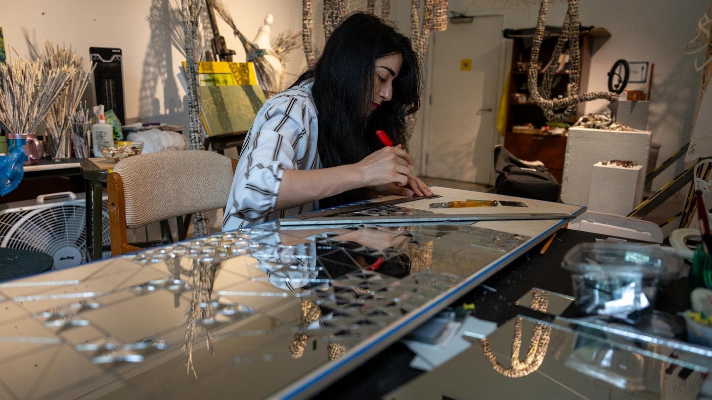 A woman works on mirror art while sitting at a table