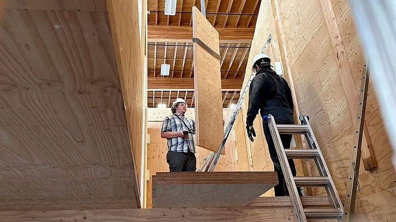 two people work on the interior of a mass plywood prototype house