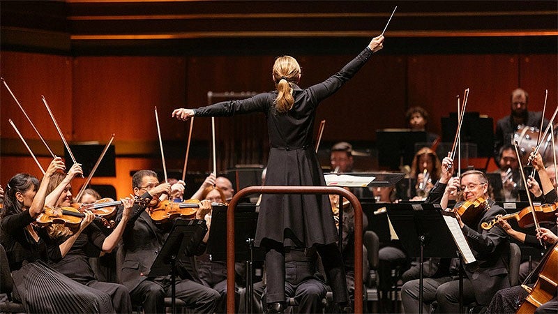 A conductor with arms raised leading an orchestra