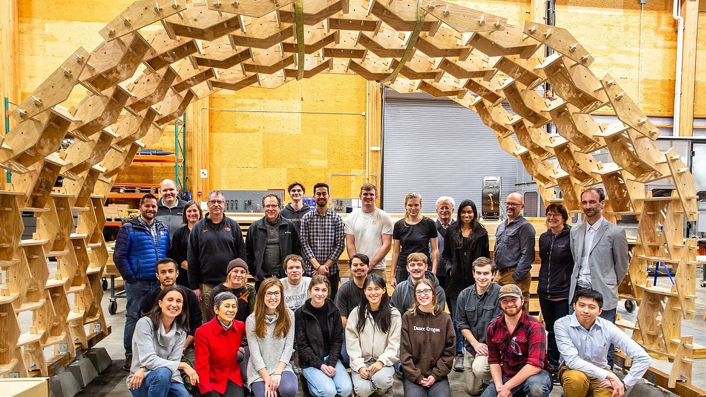 students and faculty pose underneath a wooden structure they created