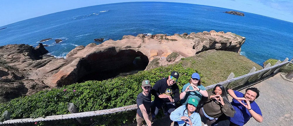 a group of people posing in front of Devil's Punchbowl on the Oregon coast