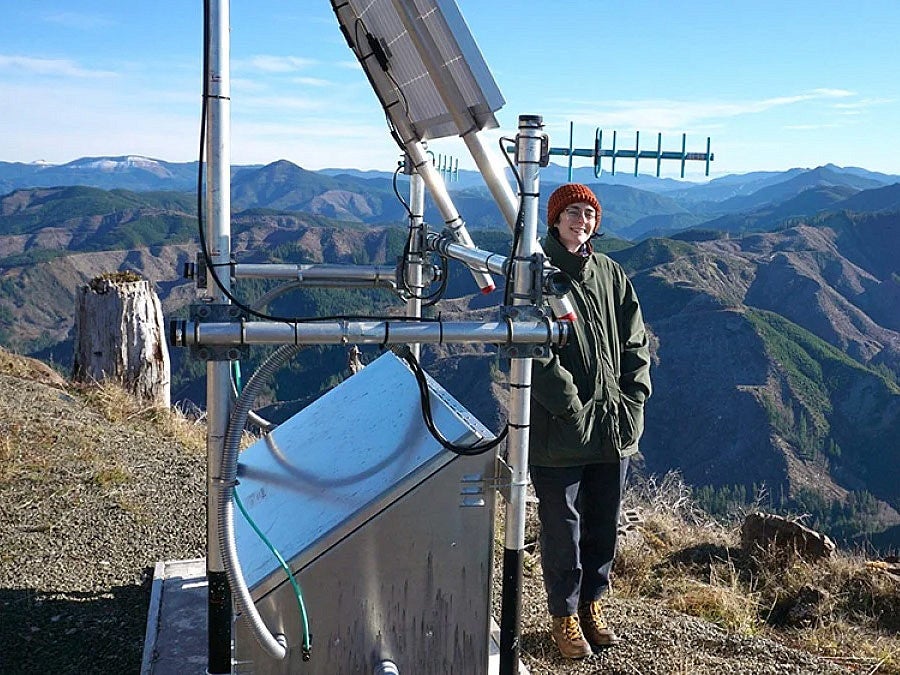 a researcher stands next to monitoring equipment on a mountain