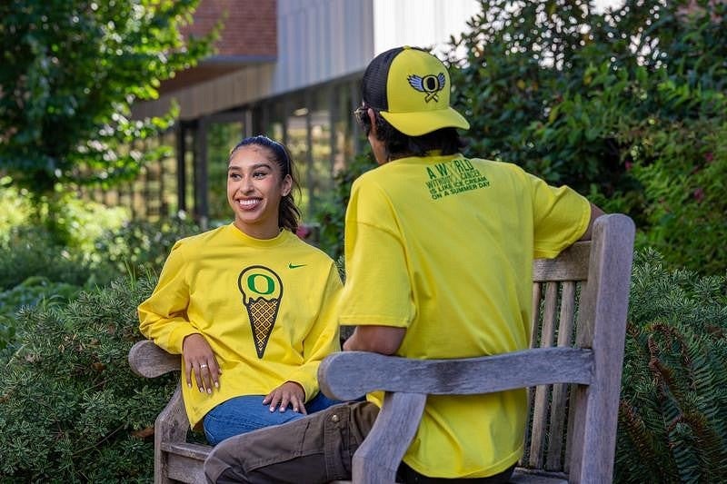 Two people sitting on a bench in apparel from the Flight and Fight collection.