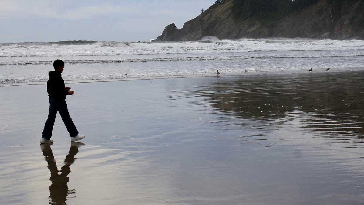 A young man walking in the surf on the beach