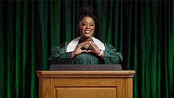 Sabinna Pierre throwing her O in her cap and gown talking behind a podium