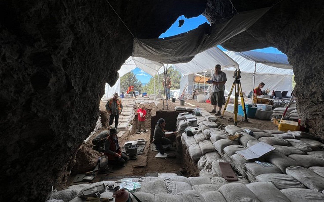 A cave entrance from the back of the cave. People are digging several feet deep and hundreds of sand bags have been stacked to create walls and stairs leading into and out of the cave.