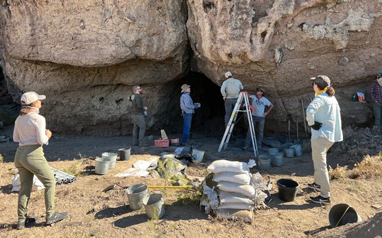 Several people stand outside a cave entrance.