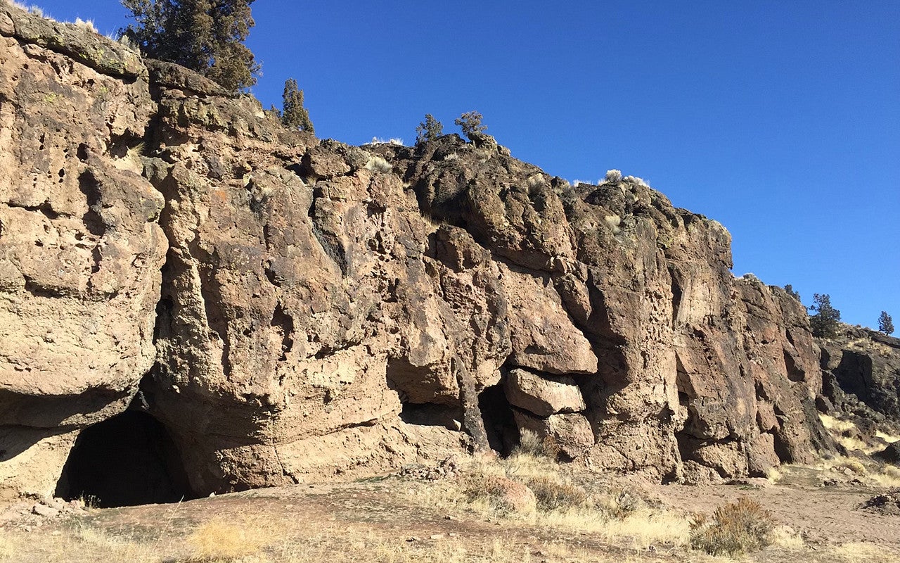 Craggy cliff face with several cave entrances against a blue sky.