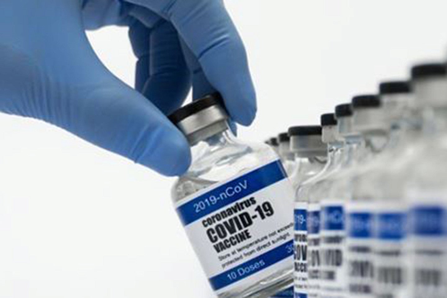 Hand wearing surgical glove selecting a vaccine bottle.