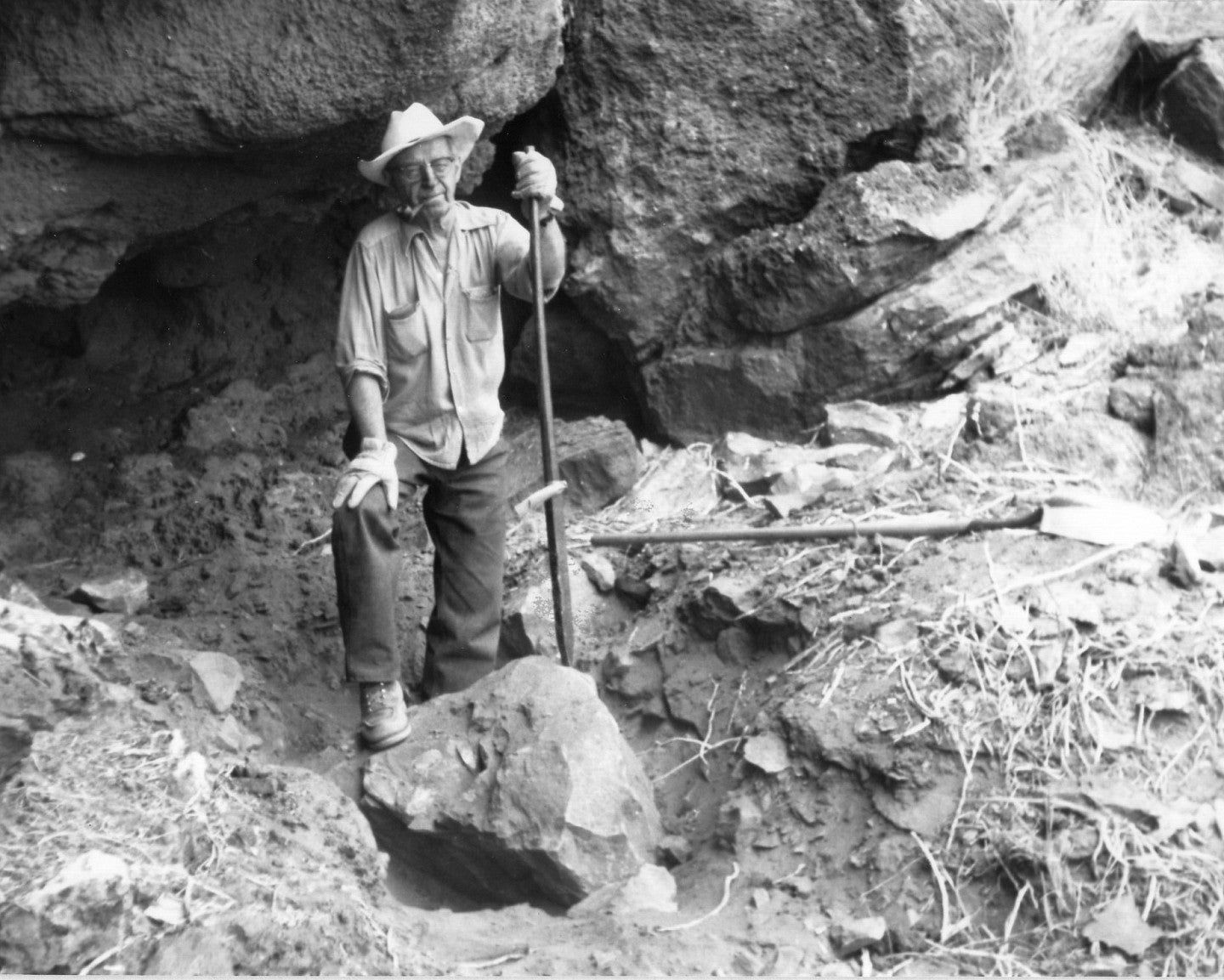 Luther Cressman smoking pipe, leaning on shovel.