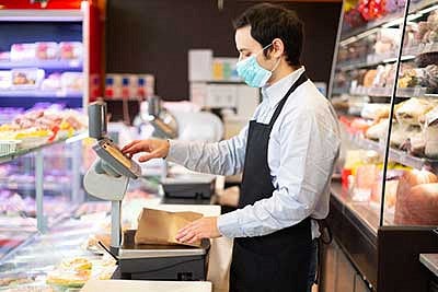 A person wearing a mask checking people out at a cafe