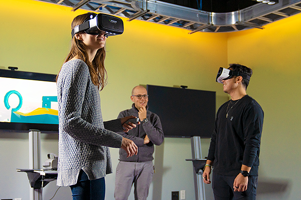 two students wear VR headsets while a professor looks on