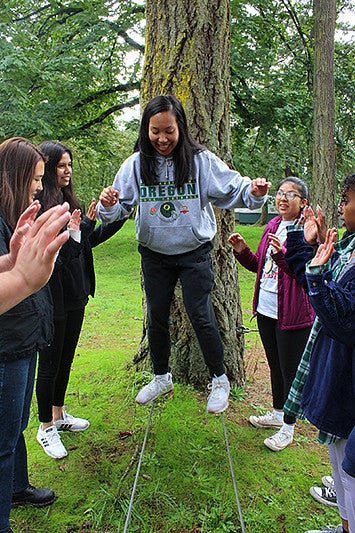 a student walks on two ropes on the low ropes course while lines of students on both sides support the student
