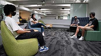 Students sitting physically distanced from each other in a residence hall wearing masks