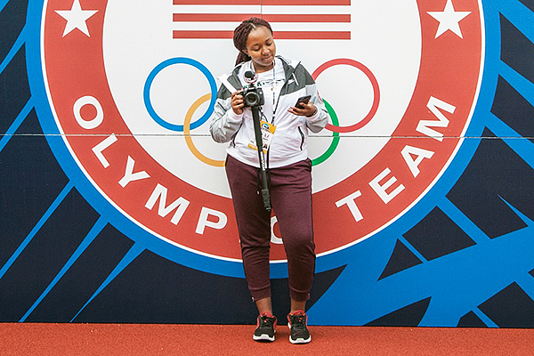 a student journalist poses in front of a US Olympic team sign