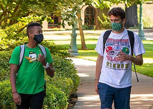 Two students walking through campus wearing masks