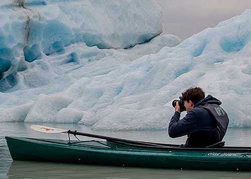 Man in a kayak taking a photo of a glacier