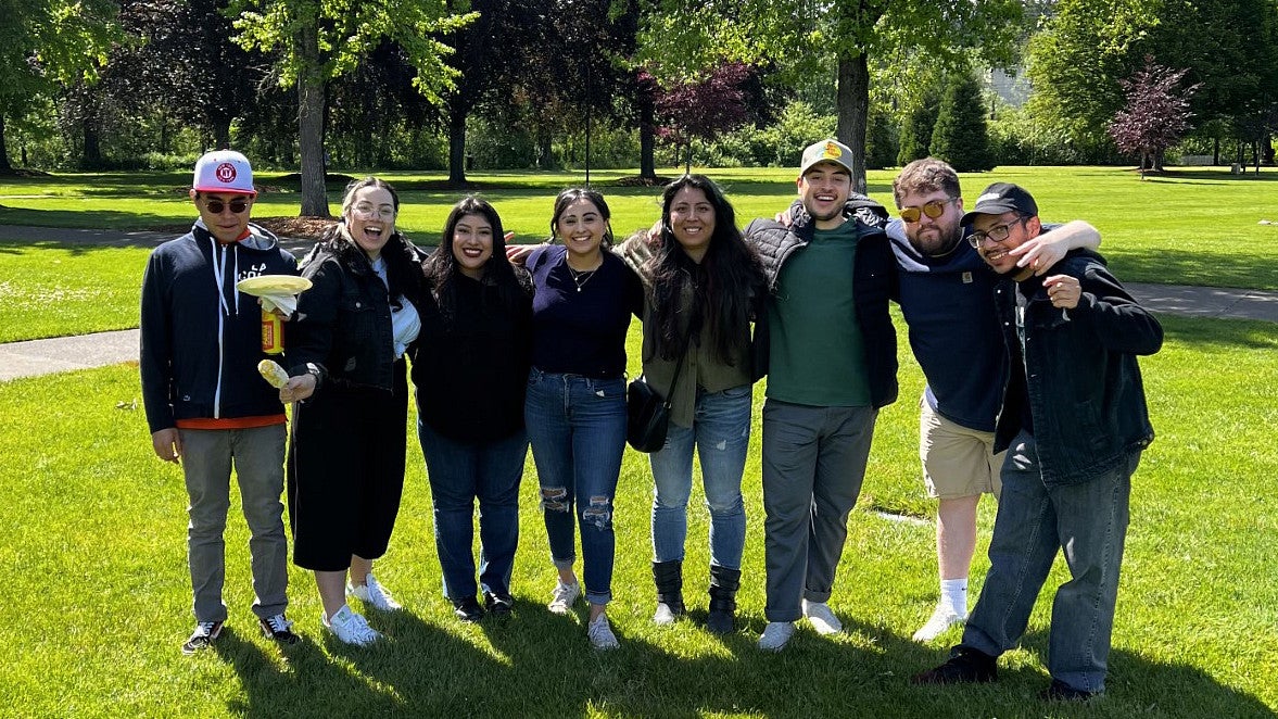 Eight men and women from the Unidos group standing together in a green park.