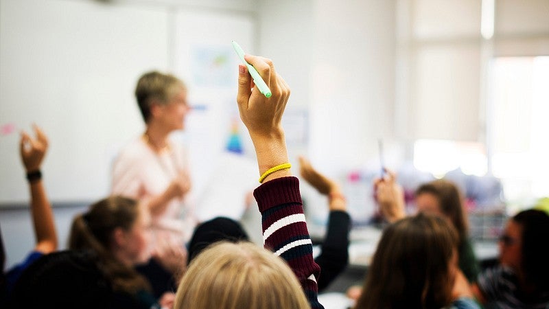 Middle school children raising their hands in a classroom