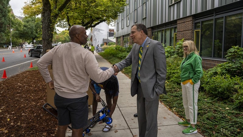 President Scholz shaking the hand of a parent during fall term move-in with a student opening a cart and Melissa Scholz watching from the side