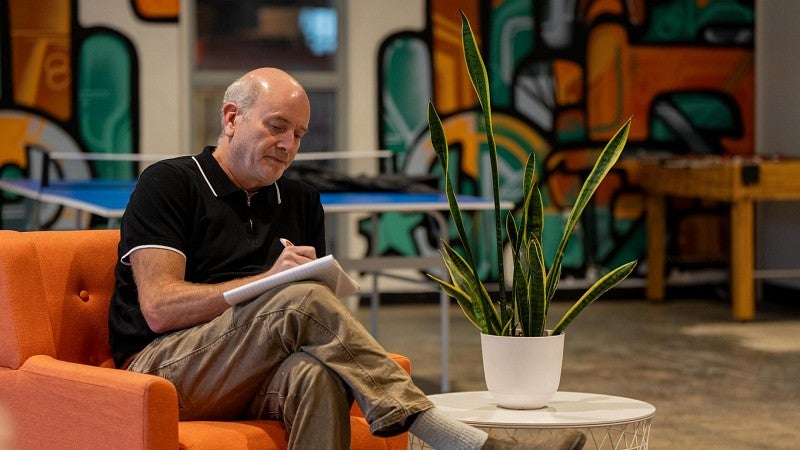 A man sitting  on an orange couch writes in a notebook.