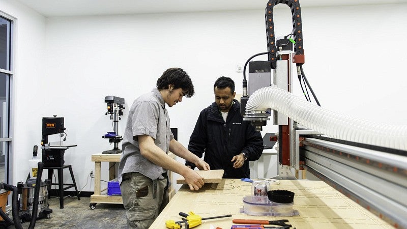 A young man learns how to use a computer-controlled industrial machine.