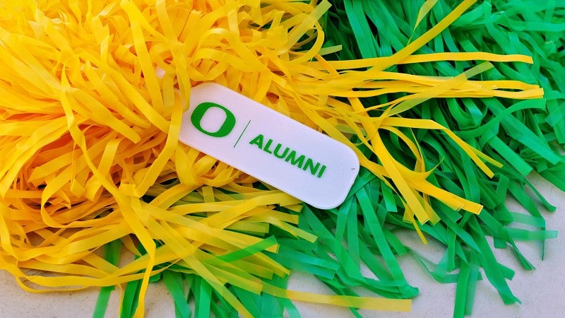 Green and yellow pom poms with a UO alumni tag