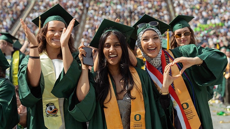 Three female graduates smiling during the UO commencement ceremony