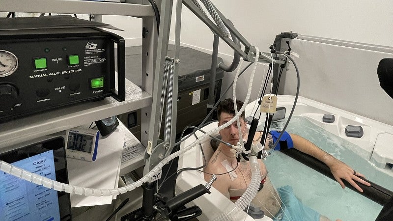 A man sits in a hot tub connected to test equipment in a university laboratory